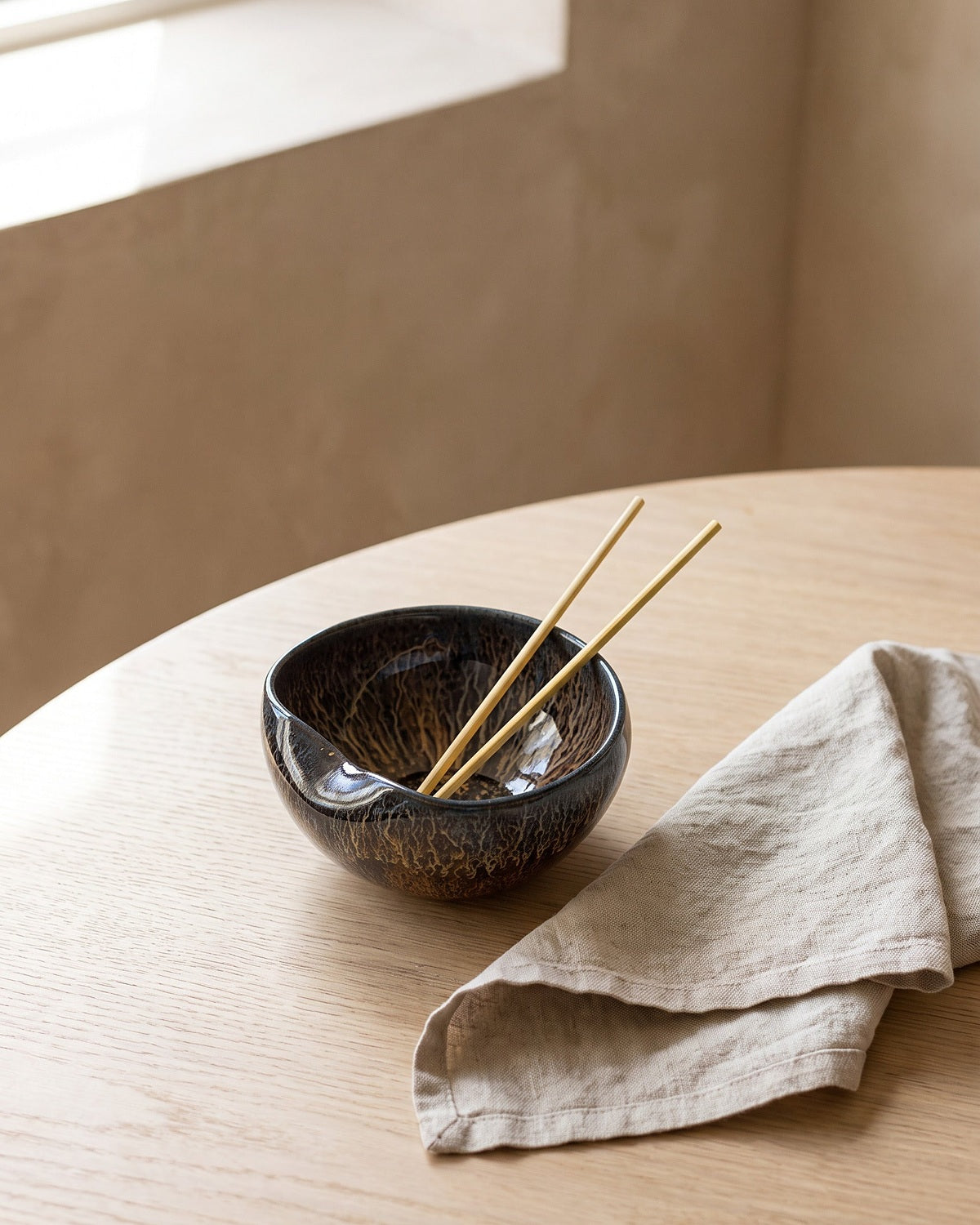 Hand-thrown ceramic bowl on linen beside a sunlit window
